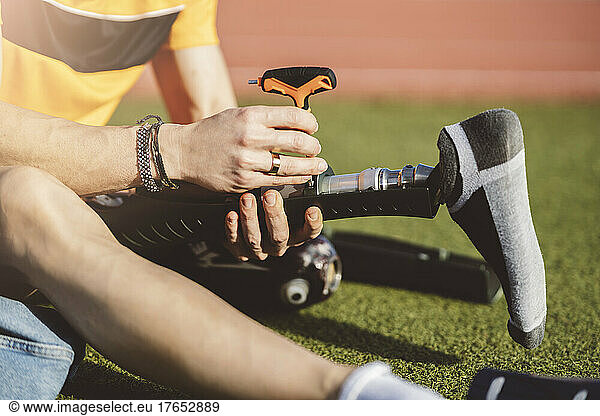 Man with disability sitting on grass adjusting prosthetic leg with screwdriver