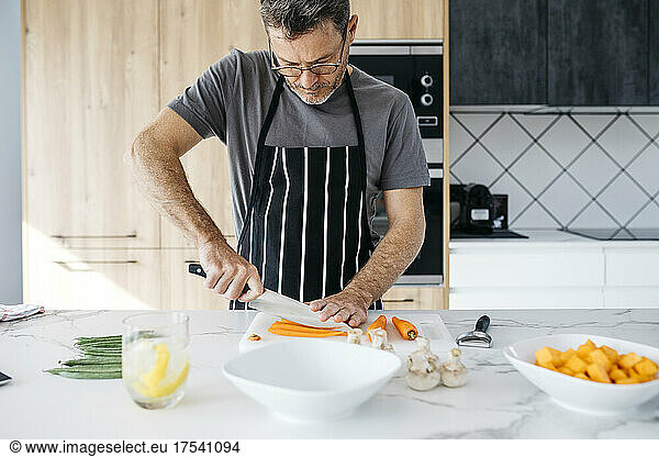 Man with eyeglasses cutting carrot on kitchen island at home
