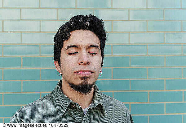 Man with eyes closed in front of turquoise brick wall