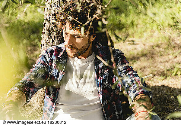 Man with eyes closed leaning on tree trunk
