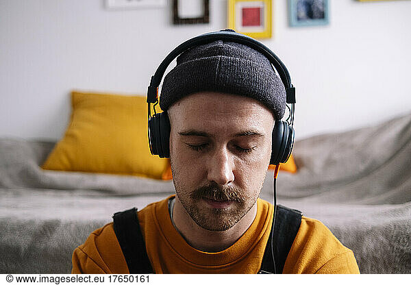 Man with eyes closed listening music through headphones at home