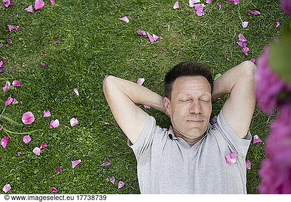 Man with eyes closed lying on grass with rose petals in garden