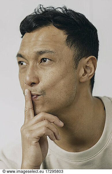 Man with finger on lips puckering against white background