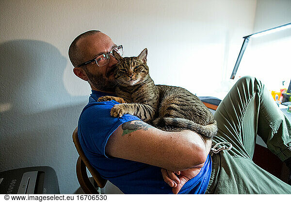 Man with glasses holds his brown tabby cat and smiles