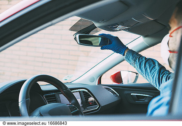 Man with gloves adjusting the mirror of his car. Drive with COVID-19.