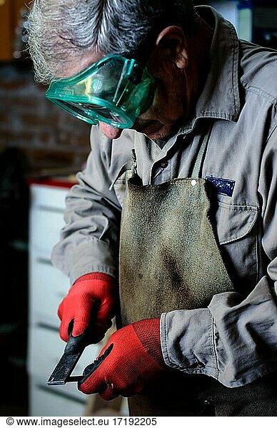 Man with gray hair and green goggles working in a workshop