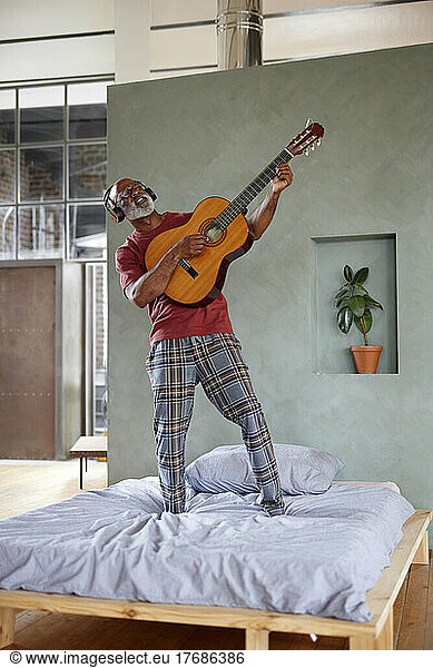 Man with guitar imitating rock musician on bed at home