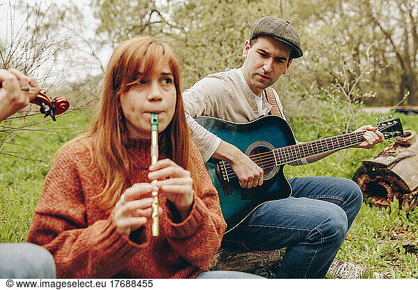 Man with guitar looking at woman playing tin whistle on field