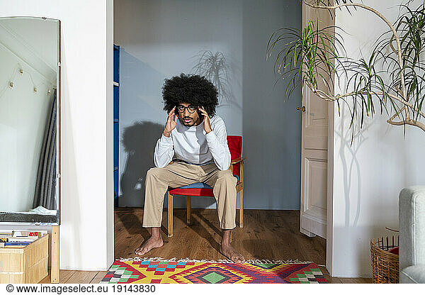 Man with hand in hair sitting on chair at home