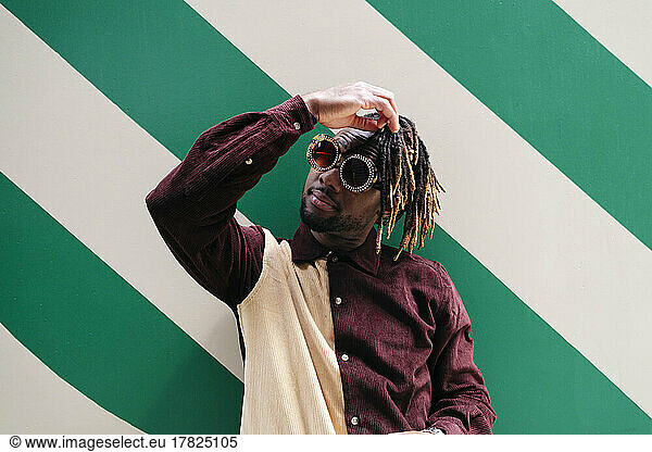 Man with hand in hair wearing sunglasses in front of green striped wall