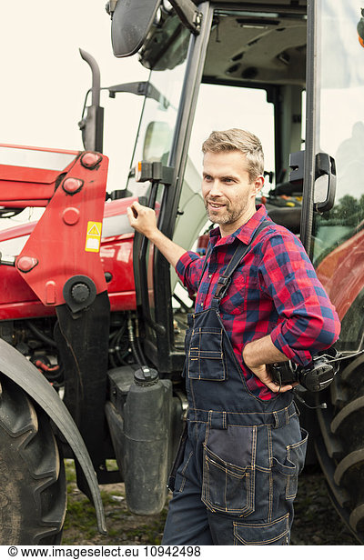 Man with hand on hip standing by tractor at farm