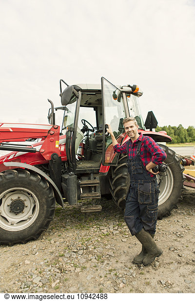 Man with hand on hip standing by tractor at farm against clear sky
