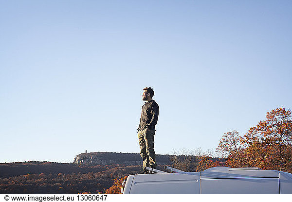 Man with hands in pocket standing on camper van against clear sky