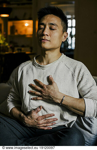 Man with hands on chest meditating at home