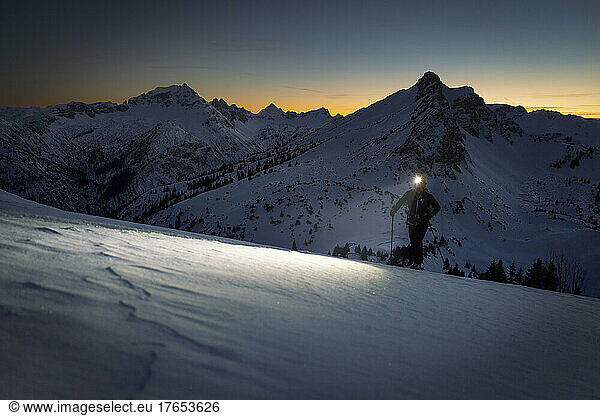 Man with headlamp walking on snowy mountain at sunset