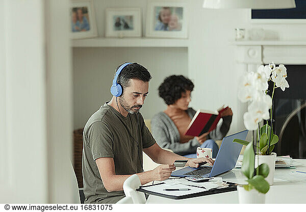 Man with headphones and credit card paying bills at laptop