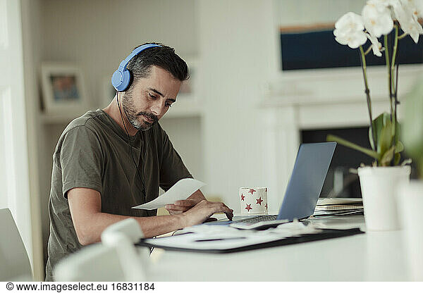 Man with headphones and receipts paying bills at laptop