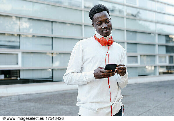 Man with headphones using smart phone on footpath