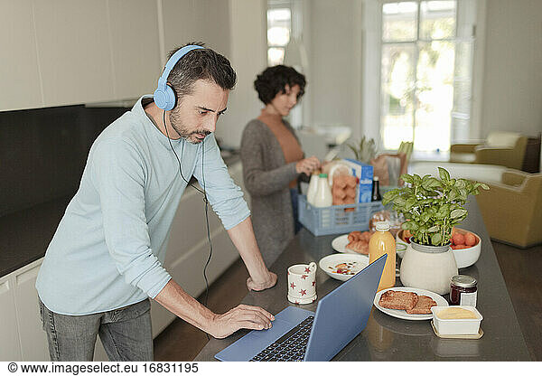 Man with headphones working from home at laptop in kitchen