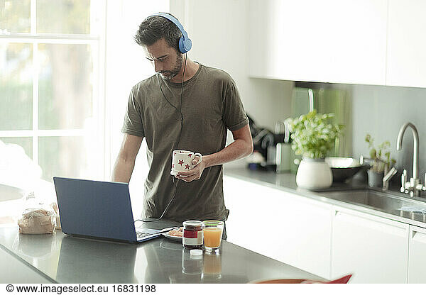 Man with headphones working from home at laptop in kitchen