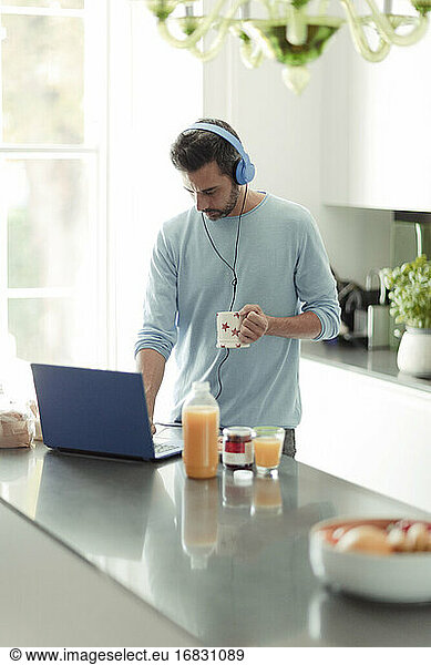 Man with headphones working from home at laptop in morning kitchen