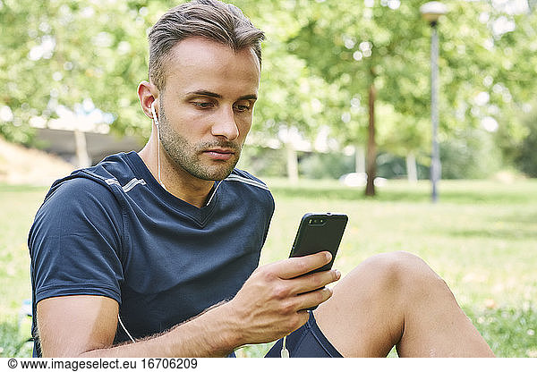 Man with his smart phone sitting on the grass in a park after training. Healthy and healthy life. Health and sport concept.