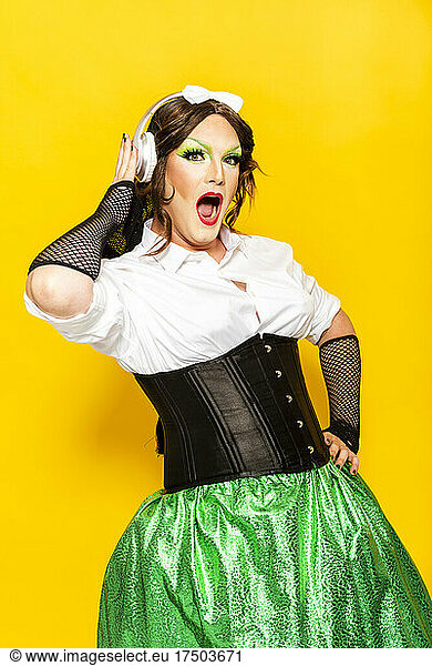 Man with make-up of drag queen dancing and shouting against yellow background