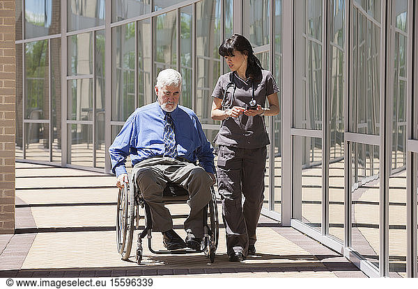 Man with muscular dystrophy and diabetes in his wheelchair walking with nurse using smart phone