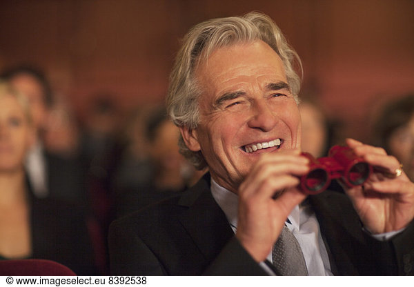 Man with opera glasses laughing in theater audience