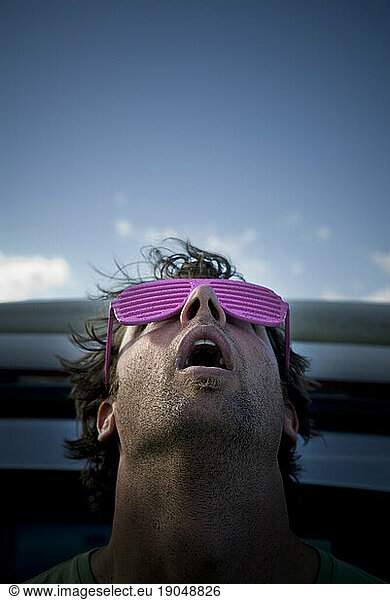 Man with pink sunglasses looks up towards blue sky  Maine.