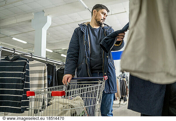 Man with shopping cart looking at clothes in store