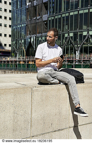 Man with smart phone sitting in front of building