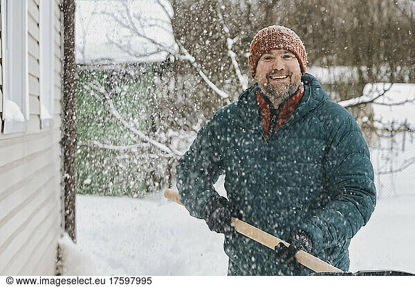 Man with snow shovel standing in snowy garden