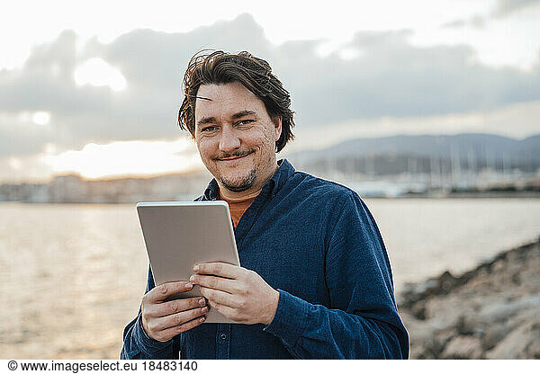 Man with tablet PC standing in front of sea