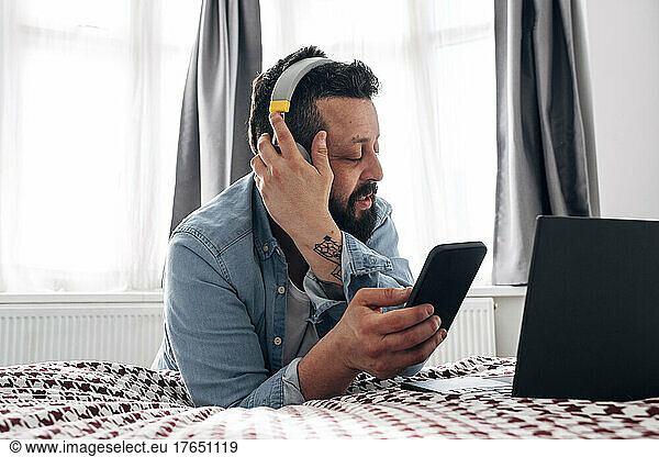 Man with wireless headphones using smart phone at home
