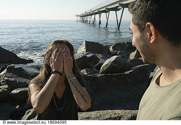 Man with young woman covering face standing in front of sea