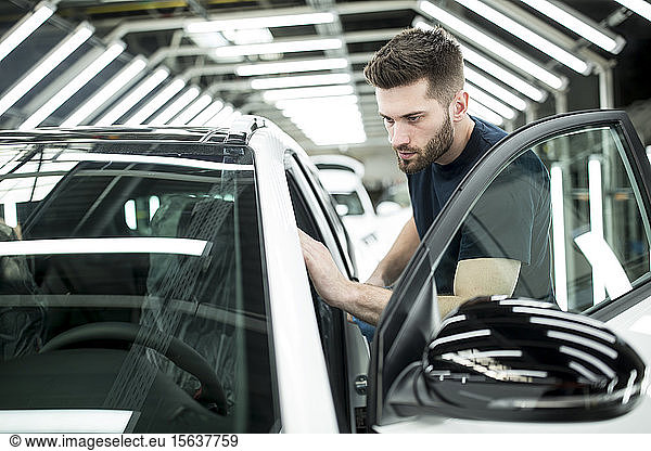 Man working in modern car factory wiping finished car