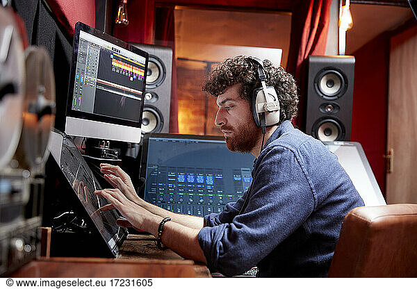 Man working in music studio using computer wearing head phones