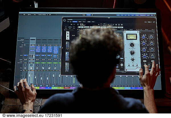Man working in music studio using large computer screen shot from behind