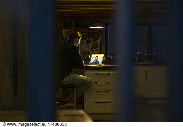 Man working late video conferencing at laptop in dark kitchen