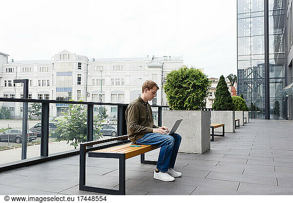 man working on laptop sitting on business center bench