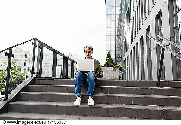 man working on laptop sitting on the stairs of business center
