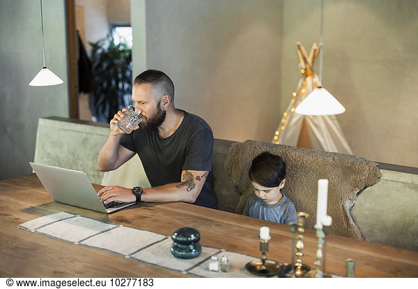 Man working on laptop while sitting with son at dining table