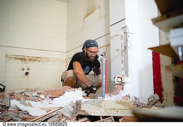 Man working on the home improvement surrounded by debris from a wall