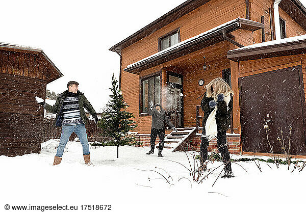 Man  young woman and adult woman playing snowballs near wooden house
