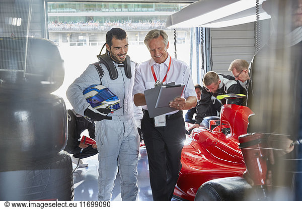 Manager and formula one race car driver talking in repair garage