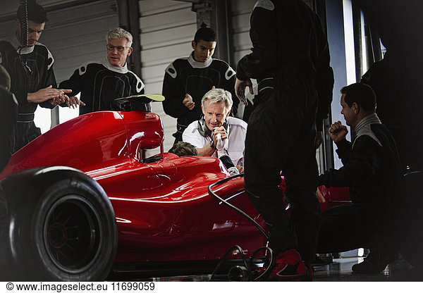 Manager and pit crew working on formula one race car in dark repair garage