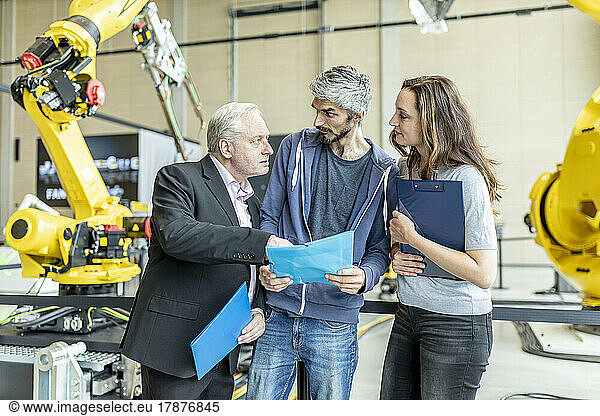 Manager discussing technical report with coworkers in front of industrial robot