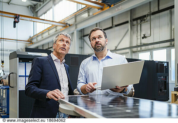 Manager holding laptop by businessman discussing at factory