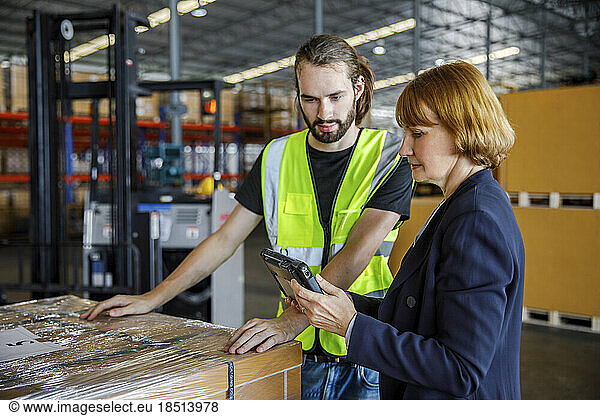 Manager sharing tablet PC with colleague by stocks in warehouse